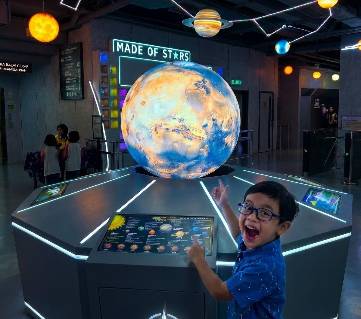 A child cheers beside the interactive LED planet sphere at Planetarium Negara